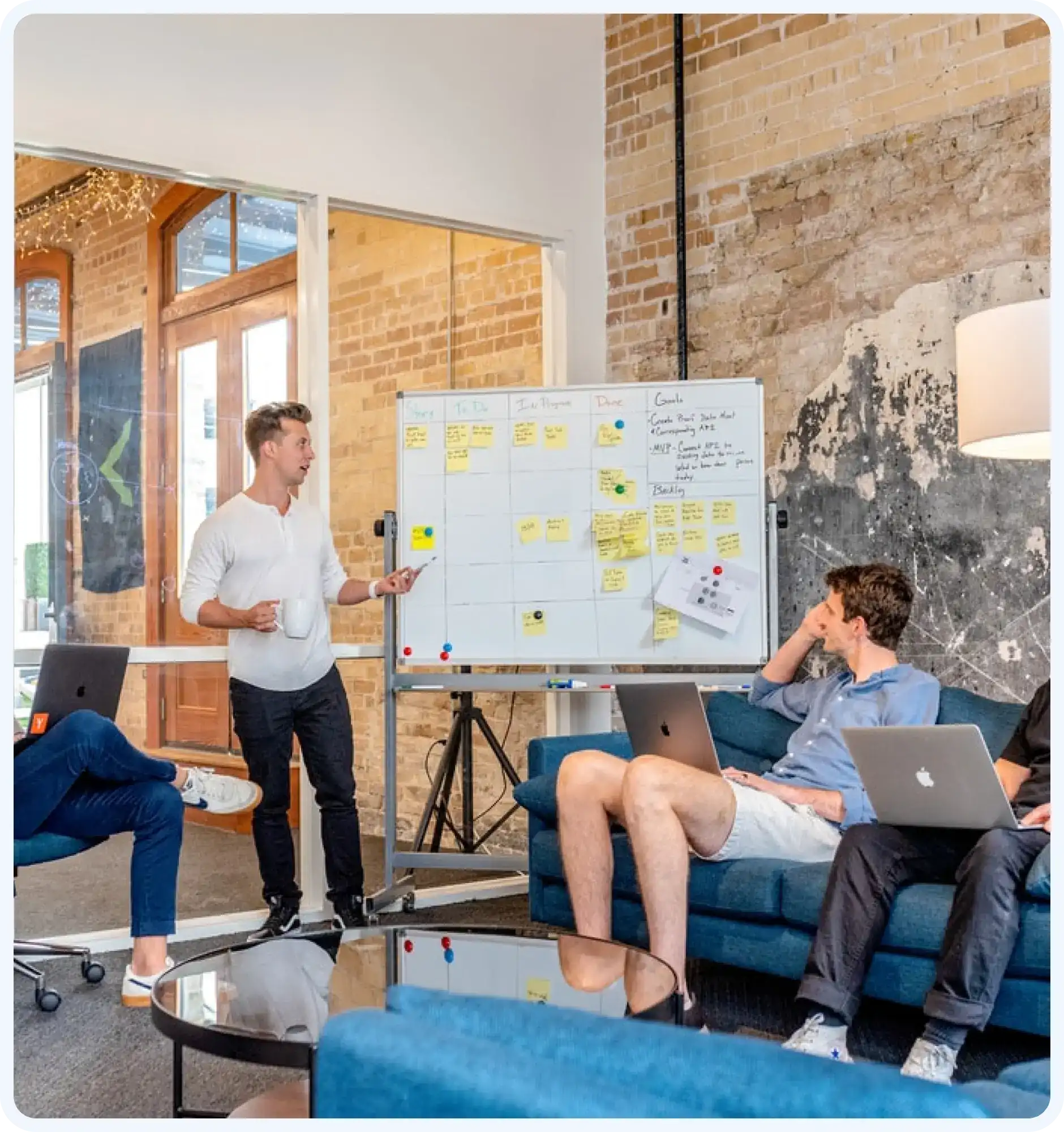 A team is discussing next steps on the whiteboard and others sitting on the couch with laptops